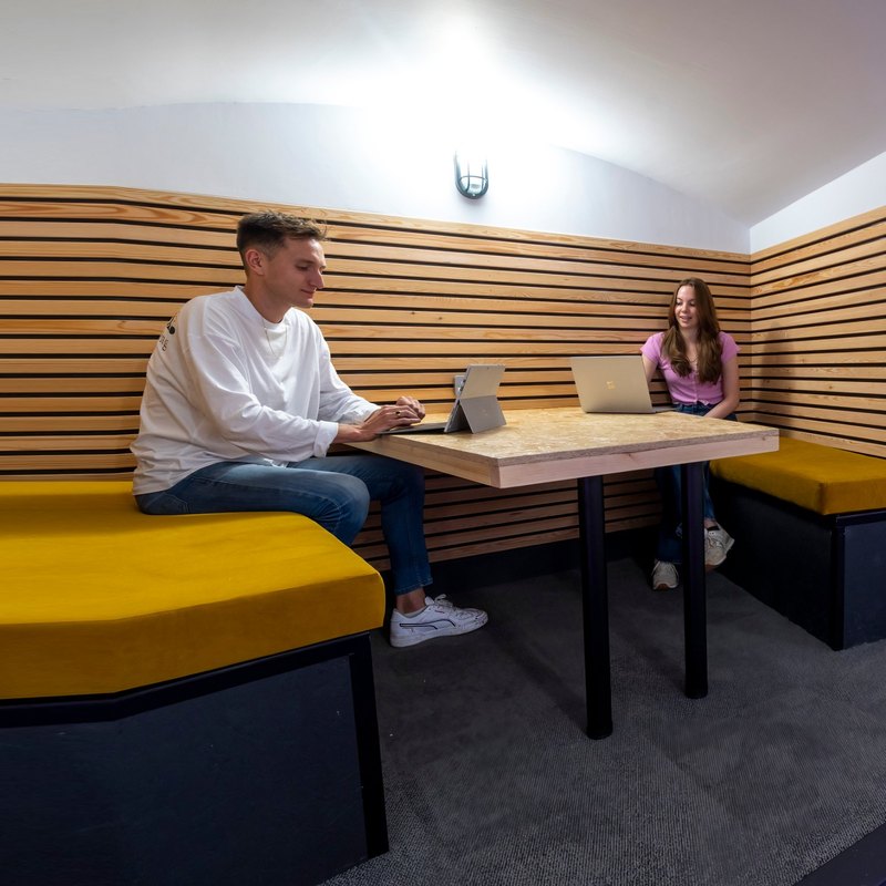 Two FMG colleagues working on laptops in a wood-panelled booth with mustard benches at Clarendon Mansions